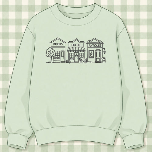 Mint green crewneck sweatshirt with green outline-embroidered storefronts reading Books, Coffee and Antiques